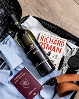 Polosladké biele víno Devín 2021 uložené v cestovnom kufri pri knihe, pripravené cestovať- rodinné vinárstvo Vinkor Malé Karpaty
