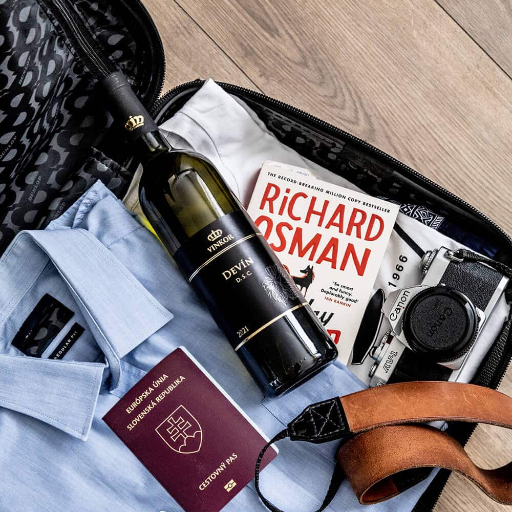 Polosladké biele víno Devín 2021 uložené v cestovnom kufri pri knihe, pripravené cestovať- rodinné vinárstvo Vinkor Malé Karpaty